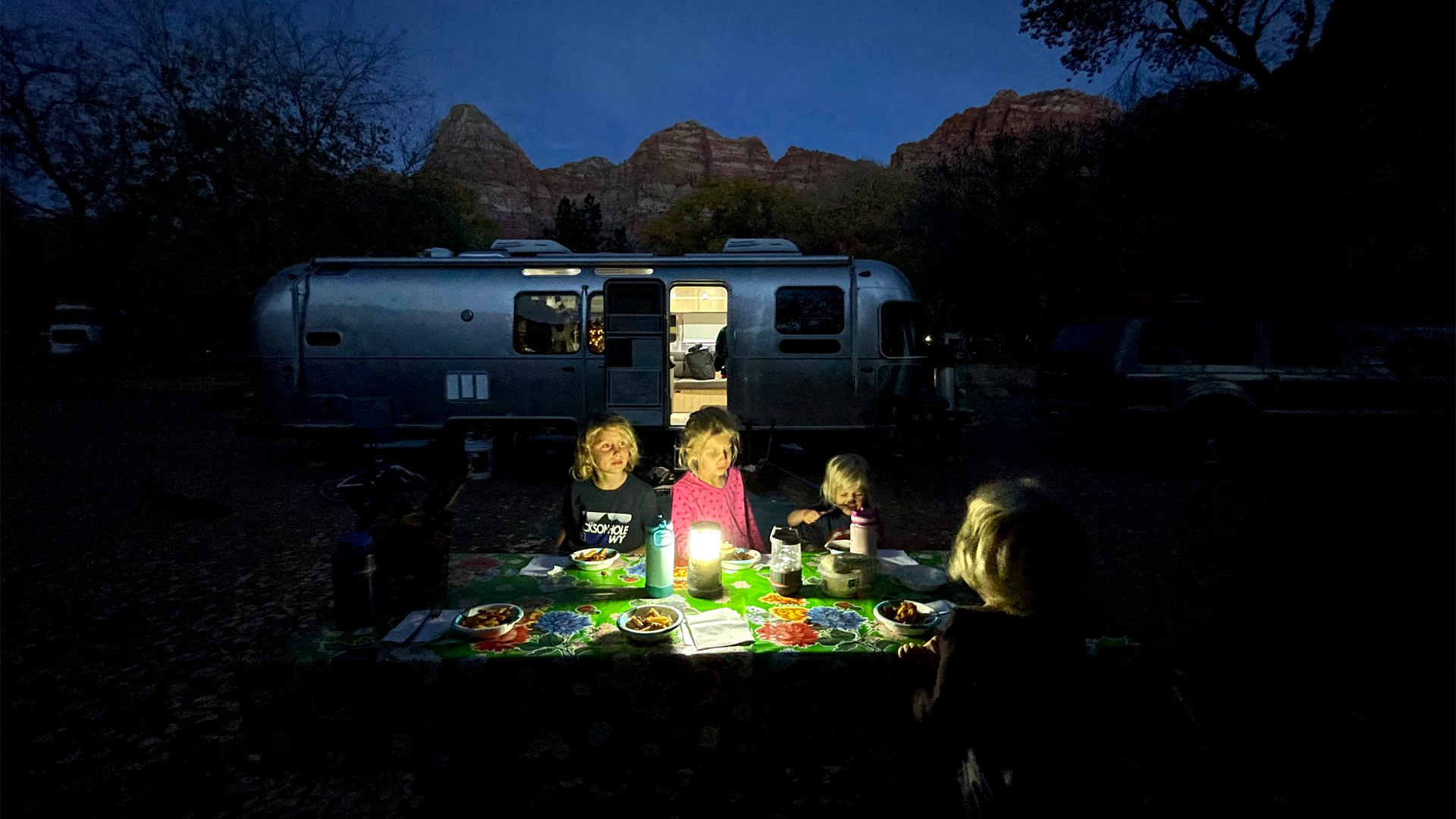 Four kids sitting around a campfire while they camp in their Airstream travel trailer.