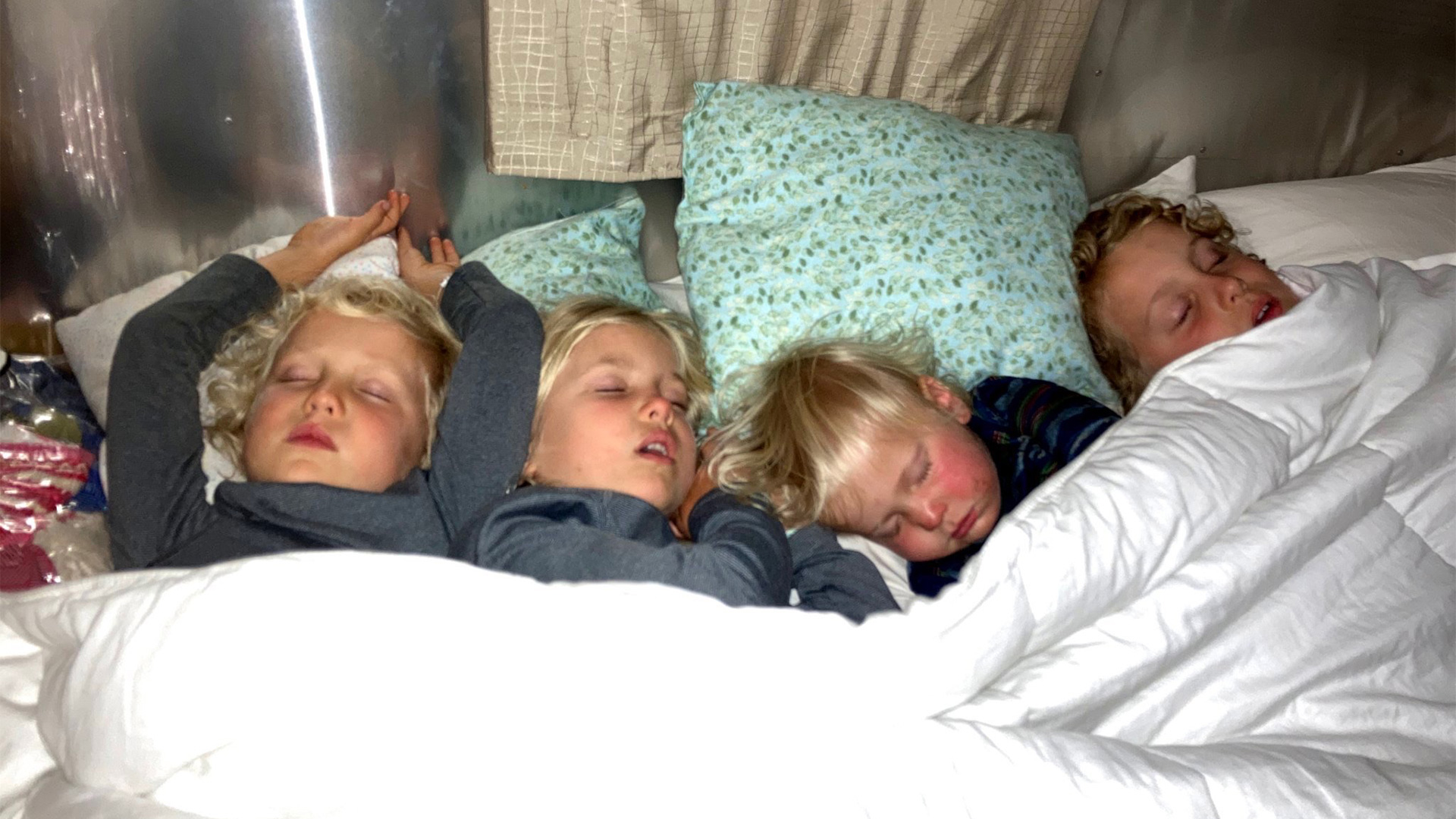Four sibling campers sleeping in an Airstream travel trailer in the same bed.