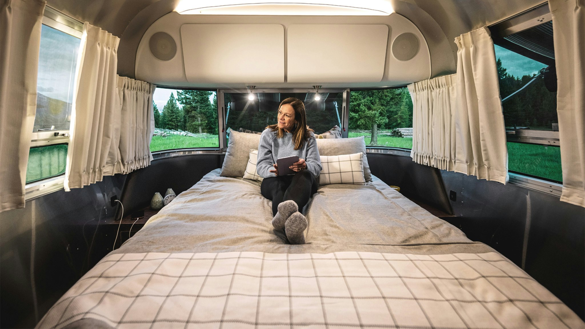 A woman camper sitting on the bed looking at her tablet in her Airstream Globetrotter travel trailer.