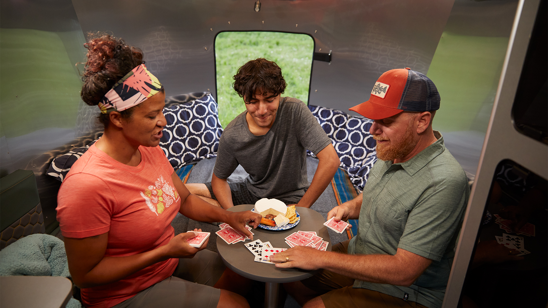 A family of campers sitting at the table playing games inside of an Airstream Basecamp travel trailer.