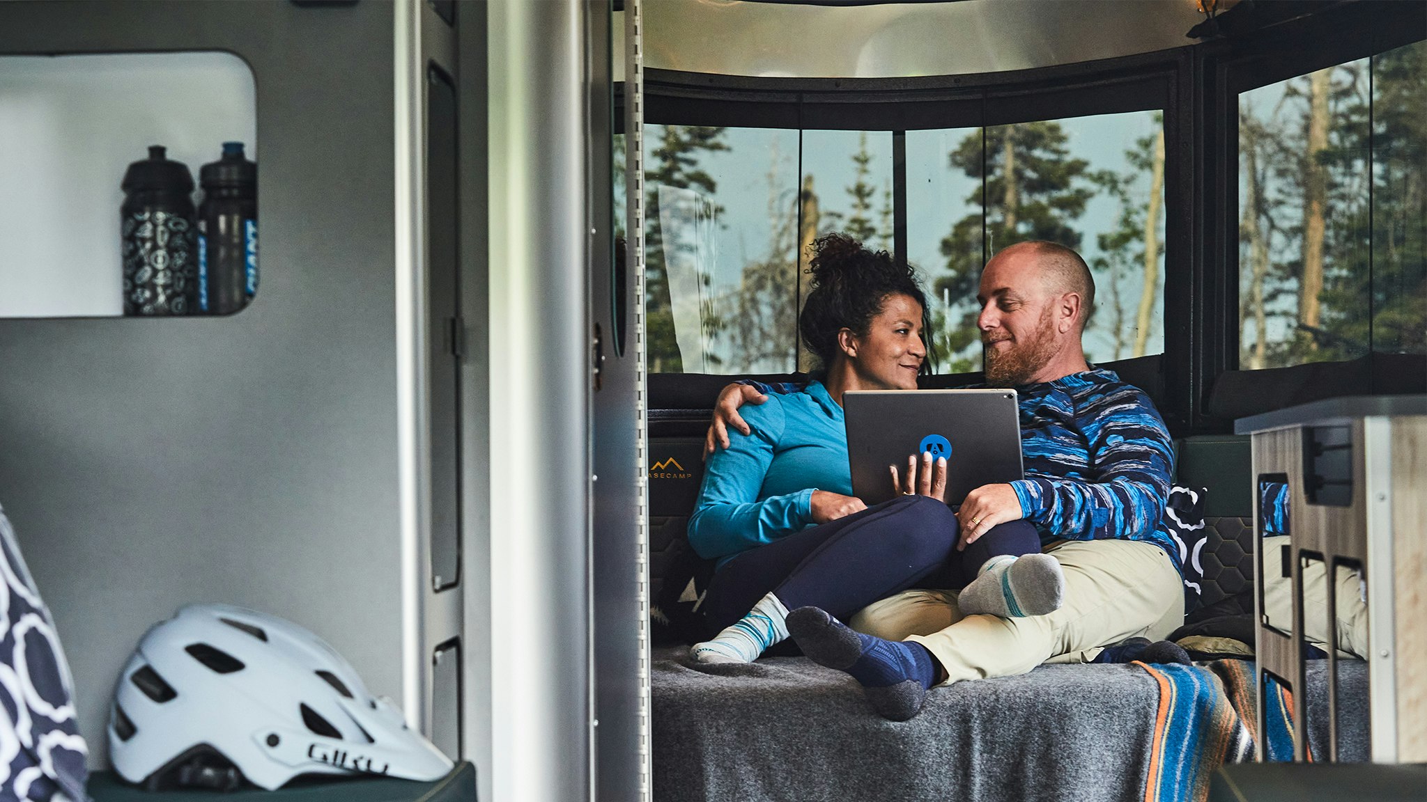 Two campers sitting on the bed of an Airstream Basecamp travel trailer watching their tablet.