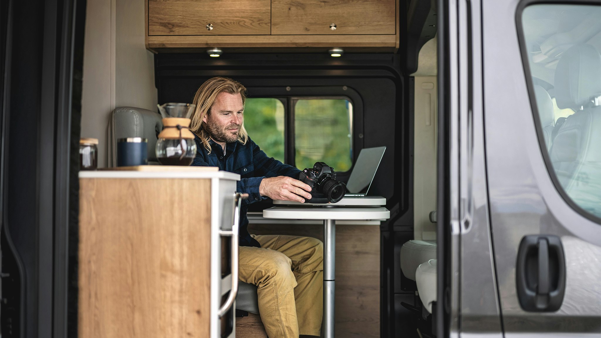 A man working on his computer and camera at the table while he is traveling in his Airstream Class B Rangeline Motorhome