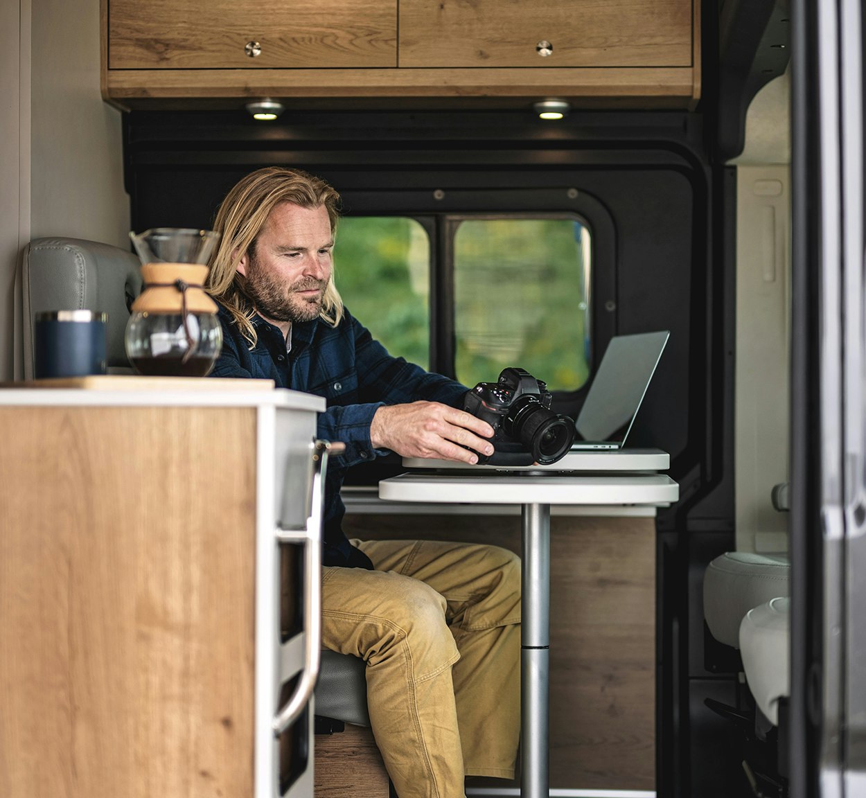 A man working on his computer and camera at the table while he is traveling in his Airstream Class B Rangeline Motorhome