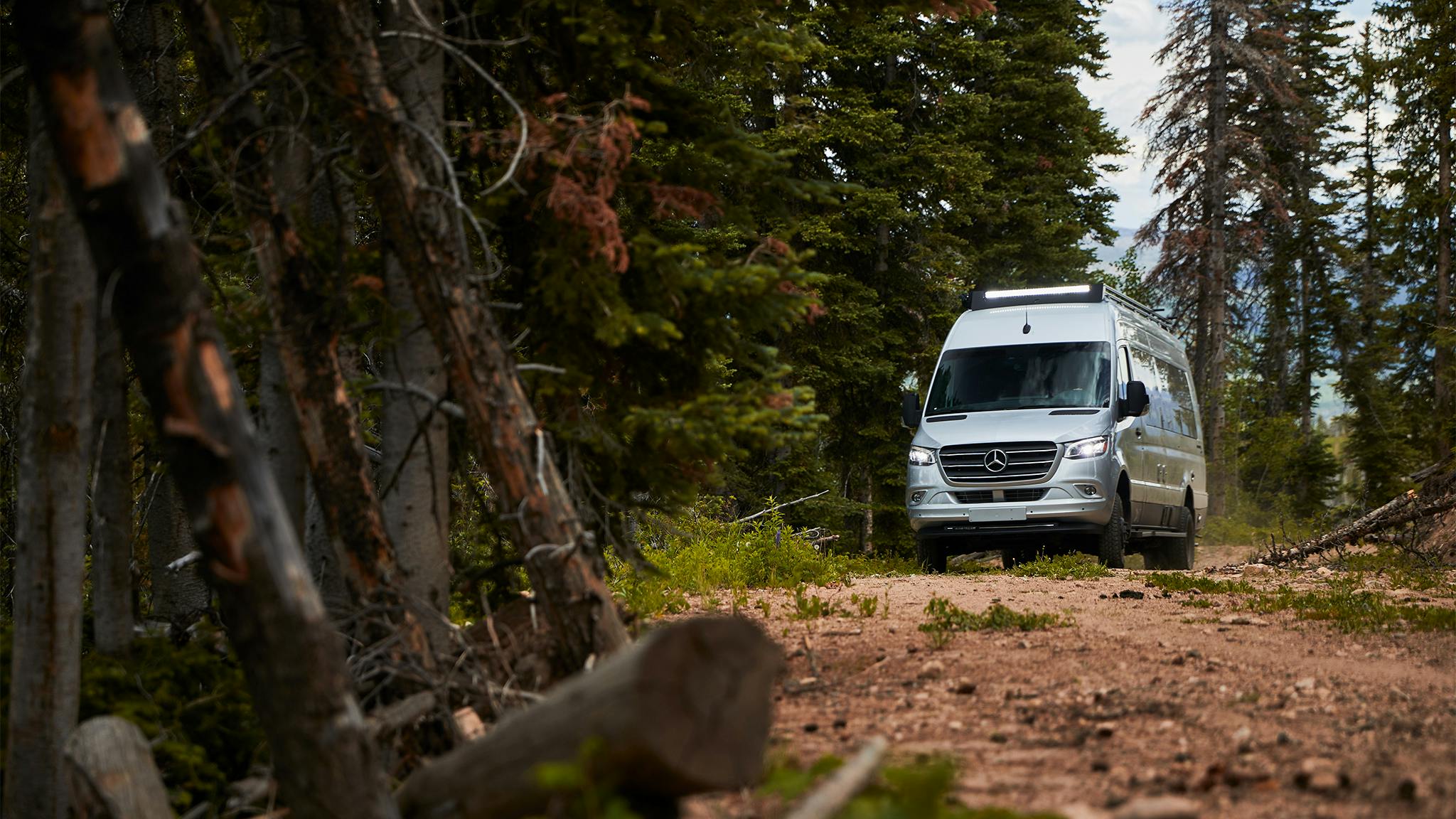 An Airstream 24X Class B Motorhome off the road driving down a dirt path through a forest.