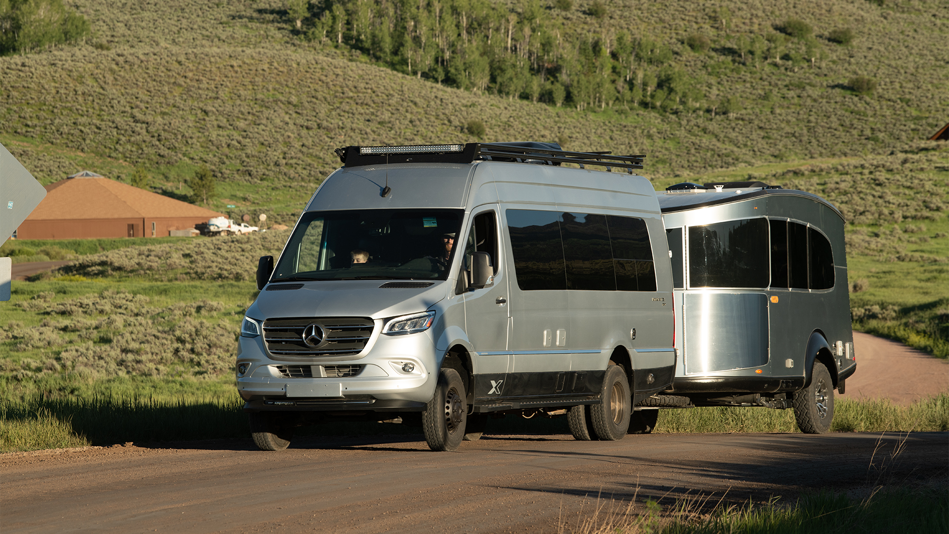 An Airstream Class B motorhome driving down a dirt road towing an Airstream travel trailer camper.