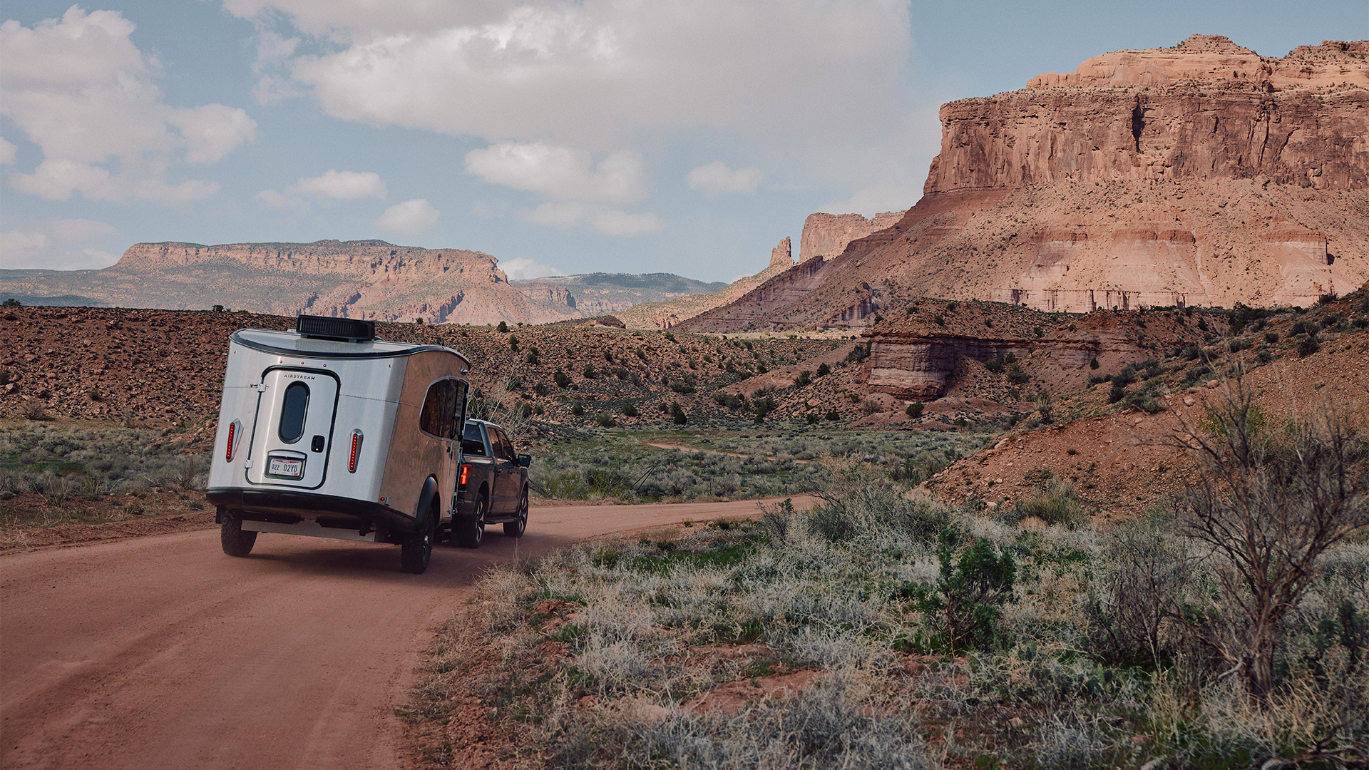 An Airstream REI Co-op Special Edition Basecamp 20X being towed down a dirt road in the desert