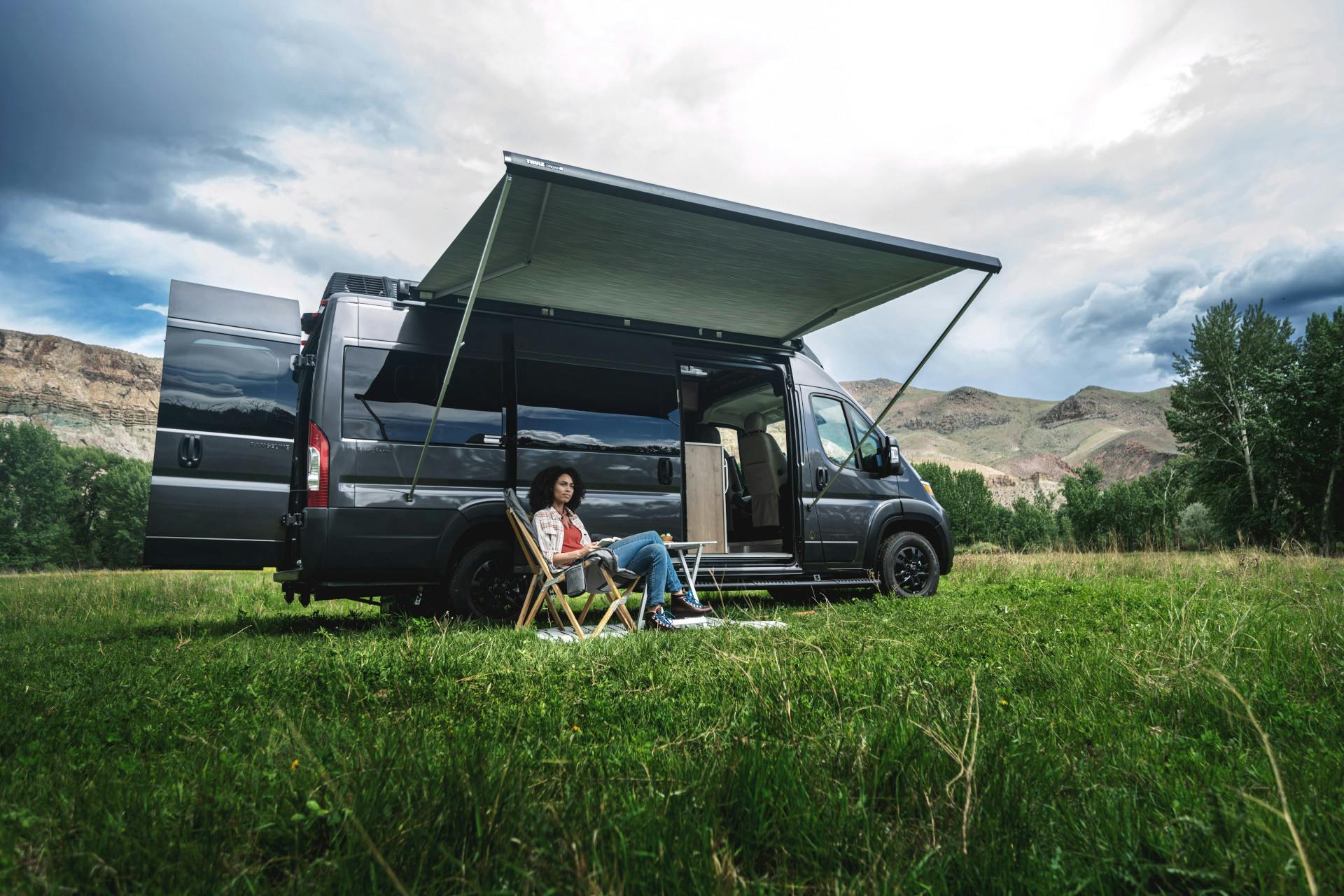 A woman sitting under the awning of her Airstream Rangeline Touring Coach