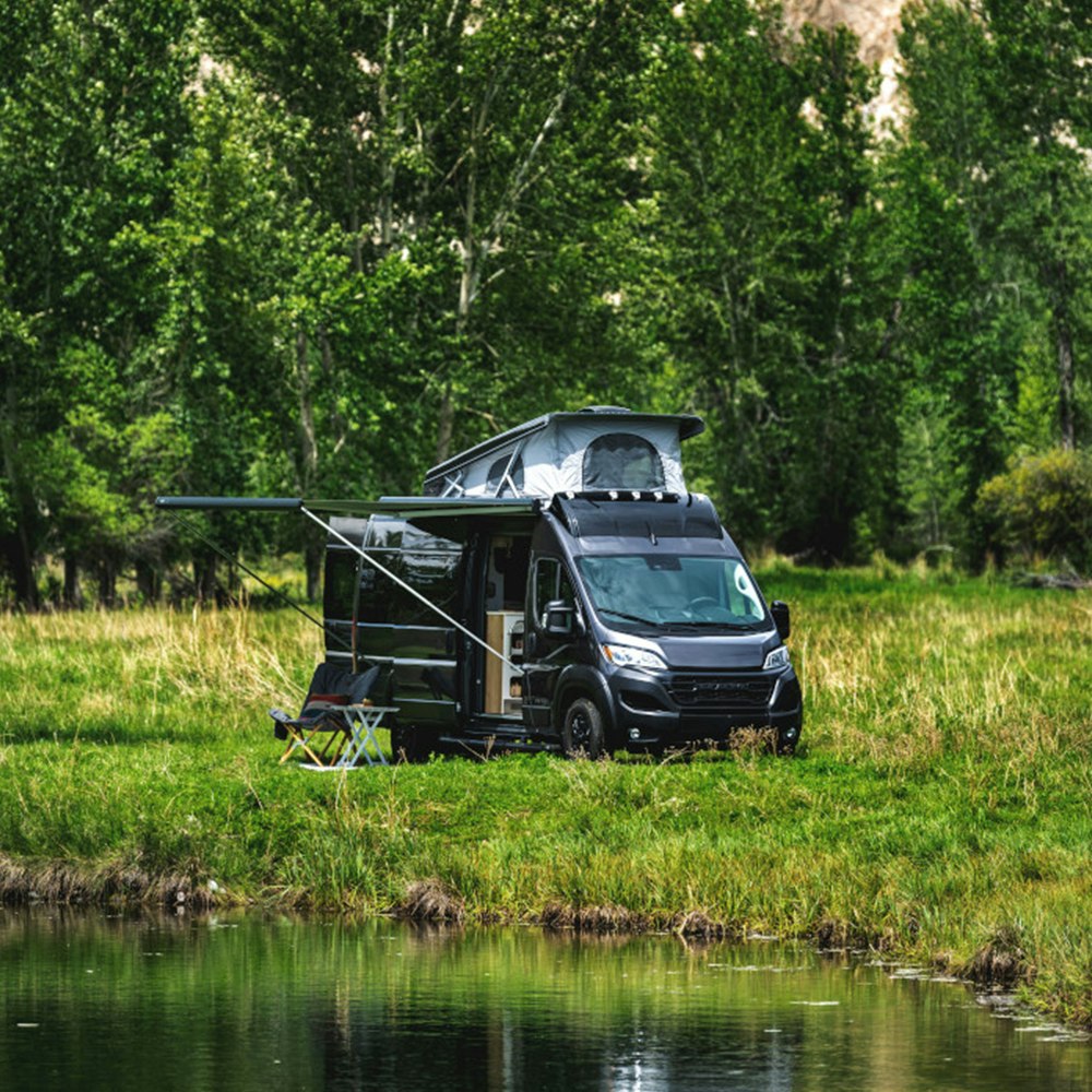 The Rangeline Touring Coach with the awning out parked in a field next to a lake.